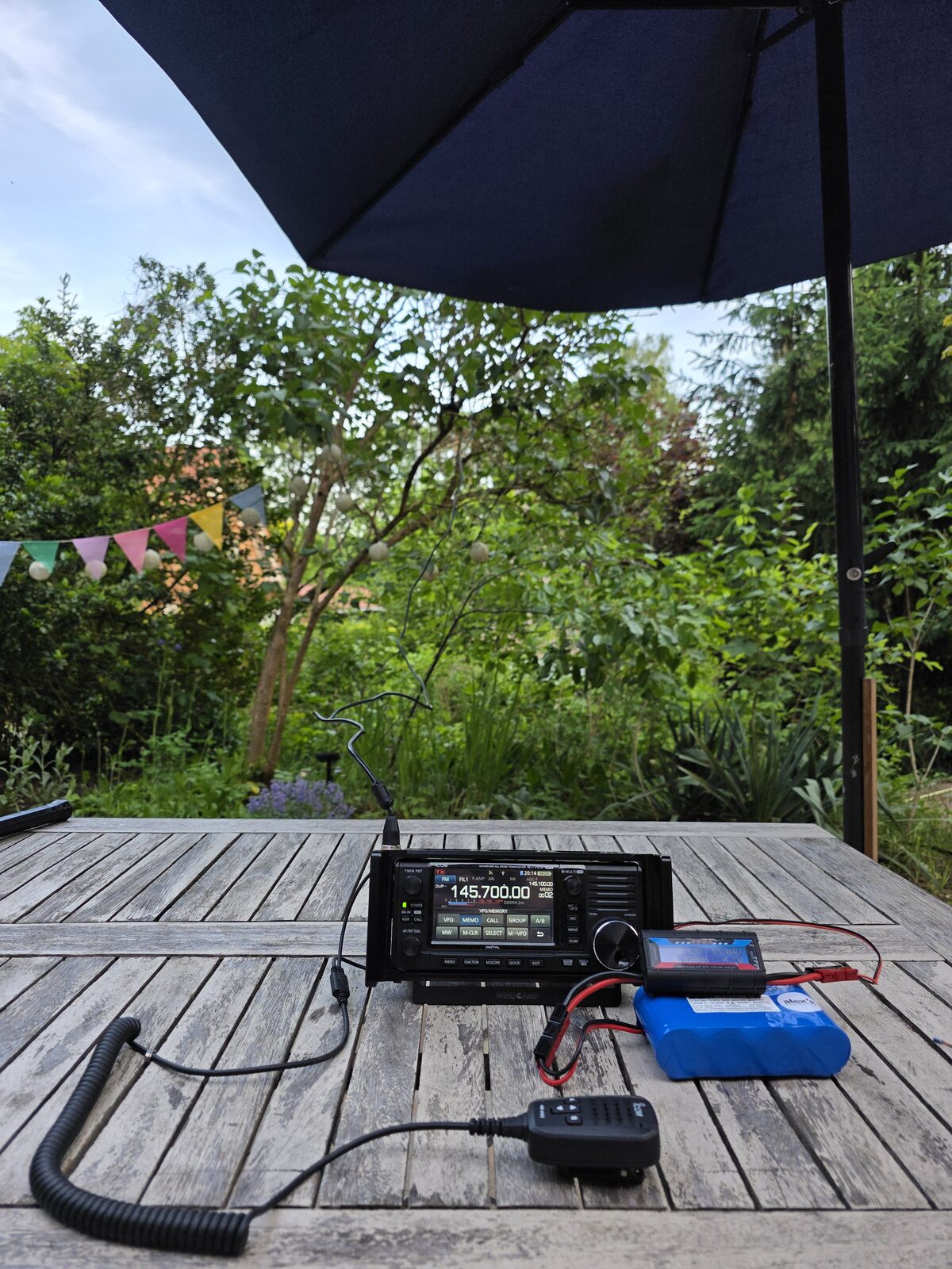 Icom IC-705 portabel auf einem Holztisch im Garten, mit externem Akku und Handmikrofon